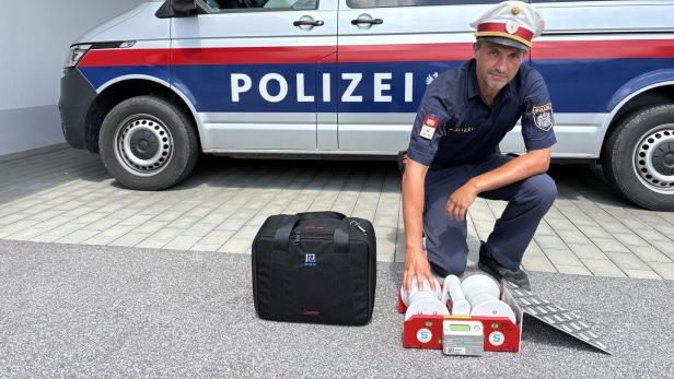 Polizist kniet vor einem Polizeiwagen neben Einsatzgerät und Tasche.
