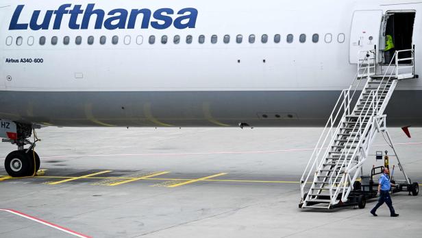 Ein Mitarbeiter geht auf dem Rollfeld an einer Lufthansa Airbus A340-600 vorbei, an der eine mobile Treppe steht.