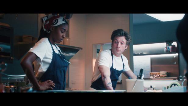 Sydney und Carmy stehen in einer professionellen Restaurantküche und unterhalten sich.