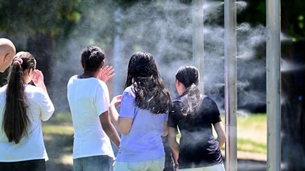 Mehrere junge Menschen kühlen sich an einer öffentlichen Sprühnebelanlage im Freien ab.