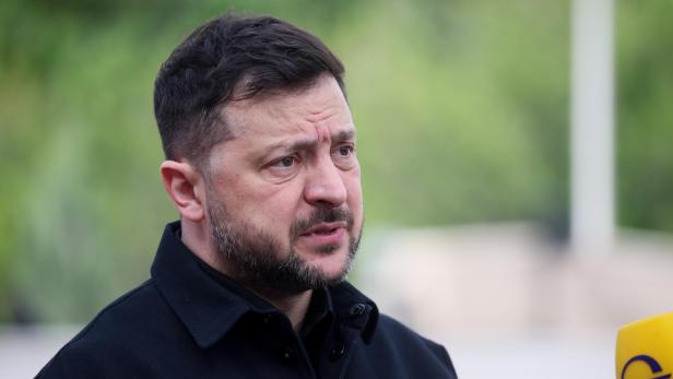 Wolodymyr Selenskyj spricht mit ernstem Gesichtsausdruck vor einem unscharfen grünen Hintergrund in ein Mikrofon.