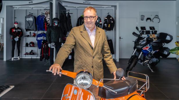 Josef Faber steht in einem Motorradladen hinter einer orangefarbenen Vespa.