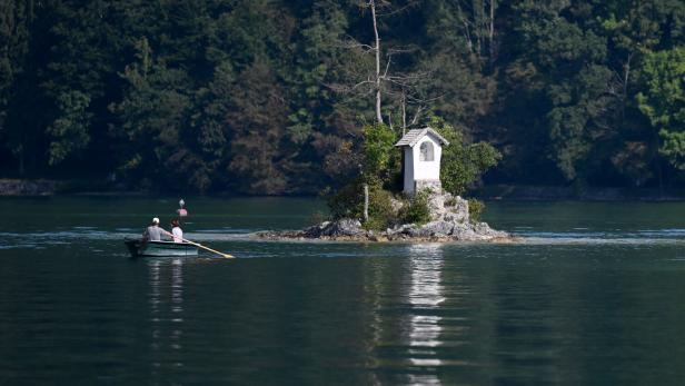 Ein Boot mit zwei Personen auf einem See neben einer kleinen Insel mit Kapelle.