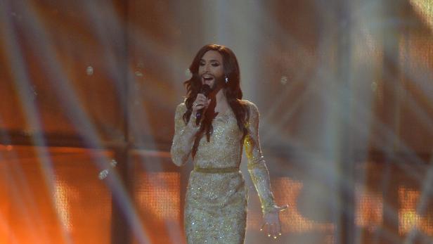 Conchita Wurst singt in einem goldenen Kleid auf einer Bühne.
