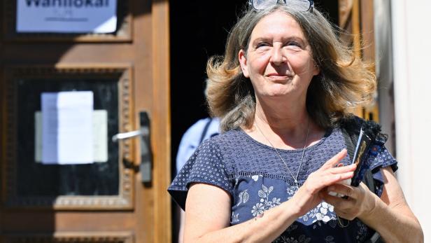 Eine Frau mit Brille auf dem Kopf verlässt ein Gebäude, an dessen Tür ein Schild mit der Aufschrift „Zum Wahllokal“ hängt.