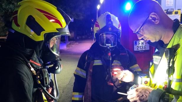 Drei Feuerwehrleute bei einer nächtlichen Einsatzbesprechung neben einem Fahrzeug mit Blaulicht.