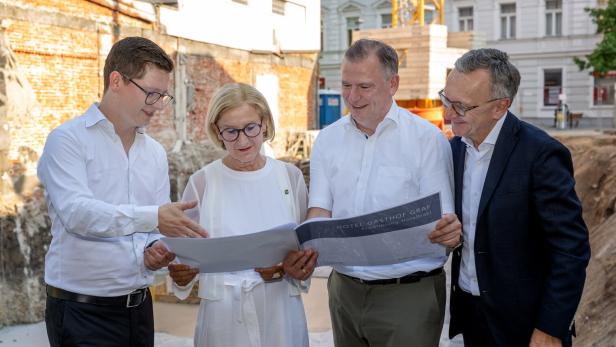 Vier Personen betrachten gemeinsam Pläne auf einer Baustelle.