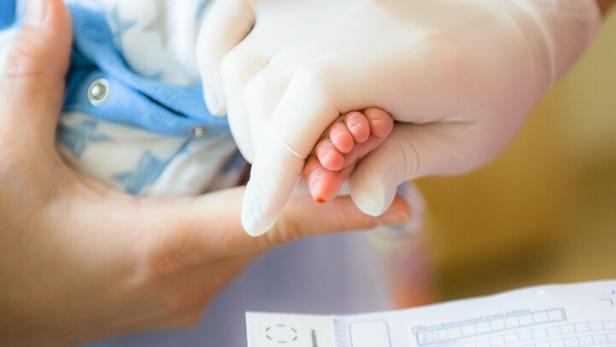 Einem Neugeborenen werden wenige Tropfen Blut aus der Ferse entnommen, diese auf eine Filterpapierkarte aufgebracht und im Labor des neugeborenen-Screeenings ausgewertet.