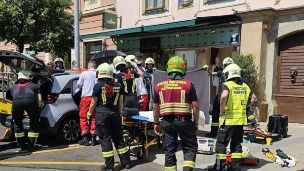Feuerwehrleute versorgen eine Person neben einem geöffneten Auto bei einem Einsatz auf der Straße.