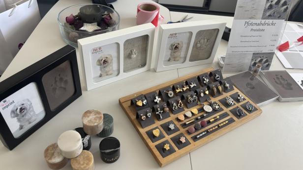 Präsentation von Pet Imprint mit Pfotenabdruck-Bilderrahmen, Schmuckstücken und einer Preisliste auf einem Tisch.