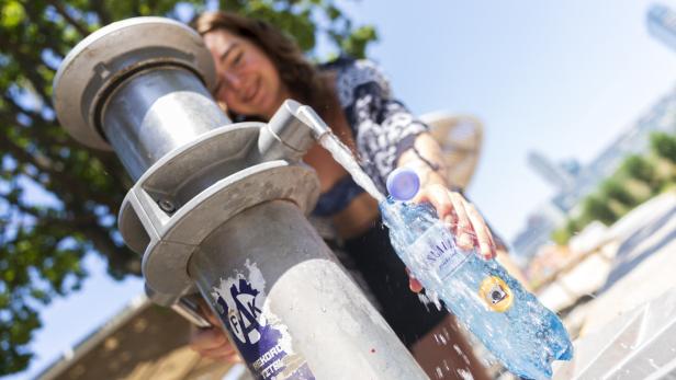 Eine junge Frau füllt an einem öffentlichen Trinkwasserbrunnen eine Plastikflasche der Marke Vöslauer auf.