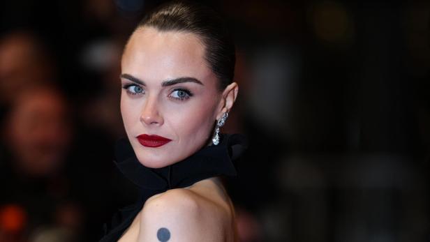 Cara Delevingne blickt mit rotem Lippenstift und hochgesteckten Haaren in die Kamera.