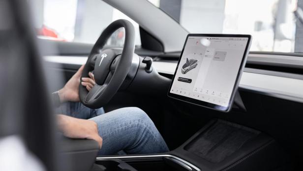Innenraum eines Tesla mit Lenkrad und großem Touchscreen.