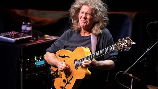 Pat Metheny spielt mit geschlossenen Augen leidenschaftlich auf einer hellbraunen Jazzgitarre vor einem dunklen Hintergrund.