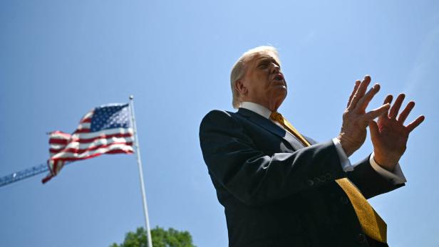Donald Trump spricht vor einer wehenden US-Flagge unter blauem Himmel.