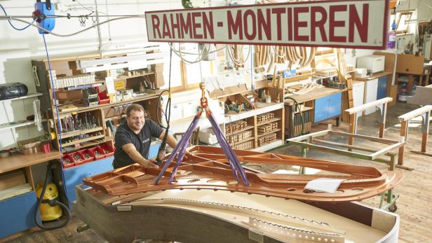 Ein Handwerker montiert in einer Werkstatt einen Flügelrahmen unter einem Schild „RAHMEN-MONTIEREN“.