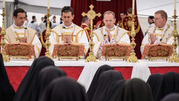Vier Priester in feierlichen Messgewändern beten am Altar vor Nonnen im Vordergrund.