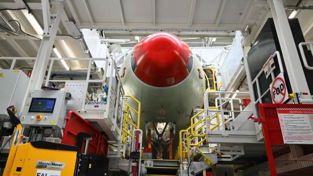 Flugzeugrumpf mit roter Nasenverkleidung in einer Industrieanlage, umgeben von Arbeitsbühnen und Maschinen.