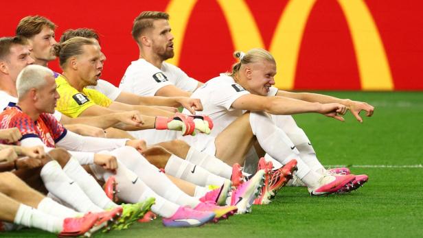 Die norwegische Nationalmannschaft jubelt sitzend auf dem Rasen. Stürmer Erling Haaland streckt seine beiden Arme aus. 