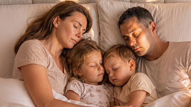 Eine Familie schläft eng aneinander gekuschelt im Bett.