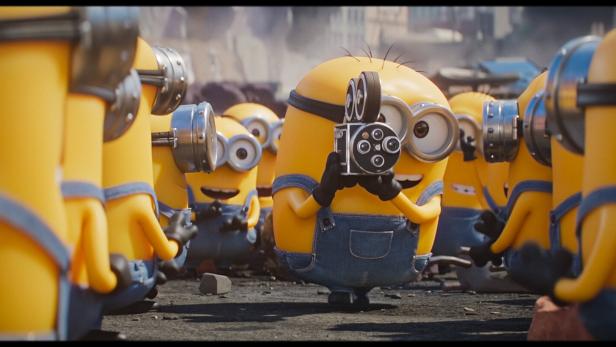 Ein Minion filmt mit einer alten Kamera, während er von weiteren Minions umgeben ist.