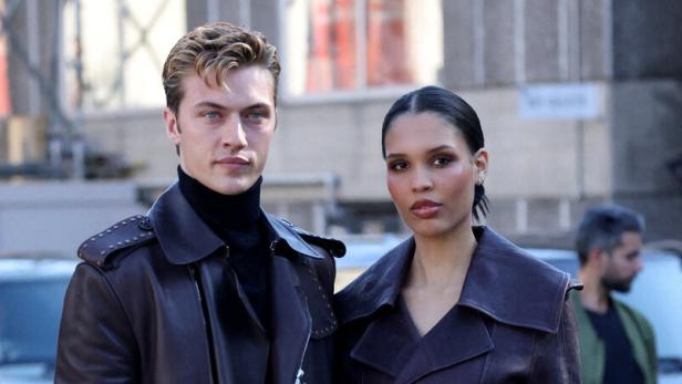 Nara und Lucky Blue Smith in eleganten, dunkelbraunen Ledermänteln posiert gemeinsam im Freien.