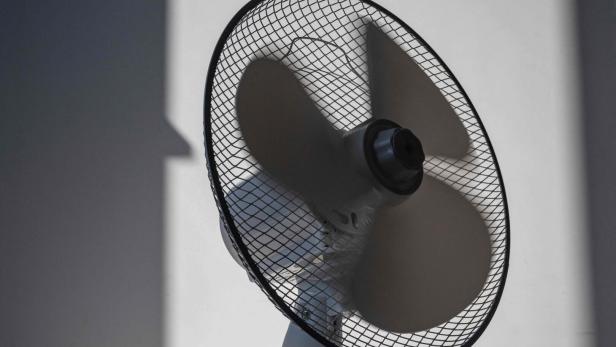 Ein schwarzer Ventilator mit Schutzgitter wirft Schatten an die Wand.