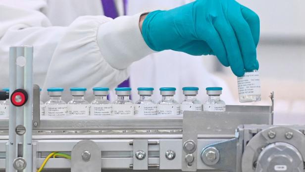 Eine Person in Laborkleidung und mit türkisfarbenen Handschuhen nimmt eine Ampulle Isatuximab von einem Fließband.