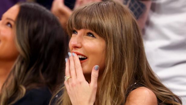 Taylor Swift lächelt freudig und hält sich die Hand vor den Mund.