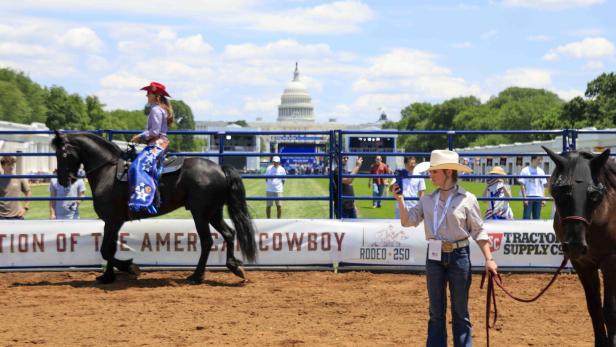 Eine Reiterin in Cowgirl-Kleidung auf einem schwarzen Pferd vor dem Kapitol in Washington, D.C. bei einer Rodeo-Veranstaltung.