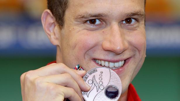 Ein lächelnder Mann hält stolz seine Medaille der Schwimm-Europameisterschaft 2012 in der Hand.