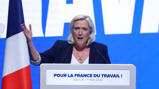Marine Le Pen spricht am Rednerpult vor französischer Flagge und Wahlkampfhintergrund.