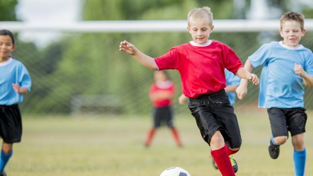 Mehrere Kinder spielen Fußball, ein Junge in Rot läuft zum Ball.