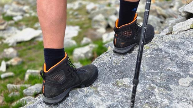 Wanderer mit Trekkingstöcken steht auf einem Felsen in den Bergen.