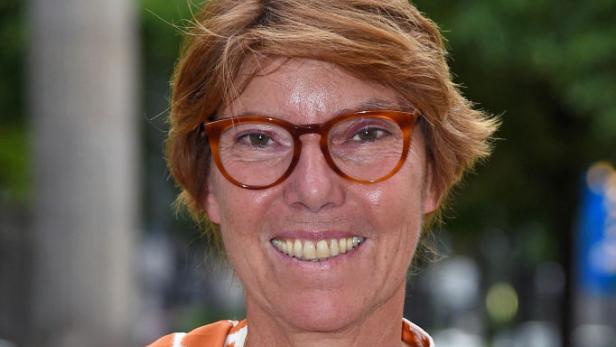 Bettina Böttinger lächelt mit kurzen roten Haaren und oranger Brille. Sie trägt eine orange-weiß gemusterte Bluse.