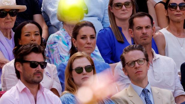 Catherine, Prinzessin von Wales, sitzt mit anderen Zuschauern auf der Tribüne, während ein Tennisball durch das Sichtfeld fliegt.