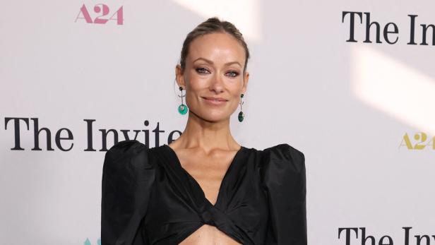Olivia Wilde trägt ein schwarzes Kleid mit Cut-out vor einer A24-Hintergrundwand.