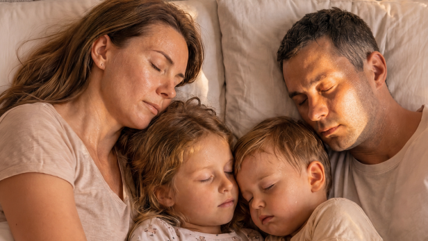 Eine Familie schläft eng aneinander gekuschelt im Bett.