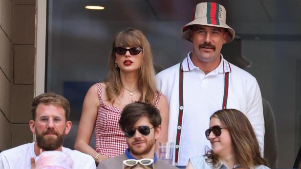Taylor Swift und Travis Kelce sitzen gemeinsam in einer Loge und schauen auf ein Sportereignis.