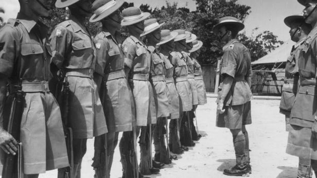 Soldaten in Uniform stehen in Reih und Glied und werden von einem Vorgesetzten auf dem Exerzierplatz inspiziert.
