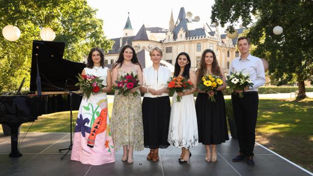 Sechs Personen mit Blumensträußen stehen vor einem Schloss neben einem Flügel im Freien.