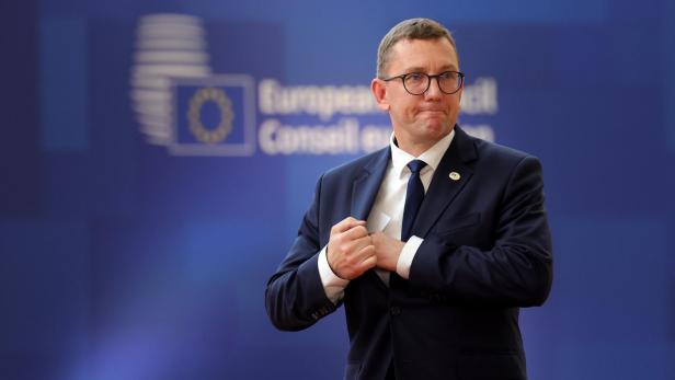 Der estnische Ministerpräsident Kristen Michal steckt vor dem Logo des Europäischen Rates etwas in seine Anzugtasche.