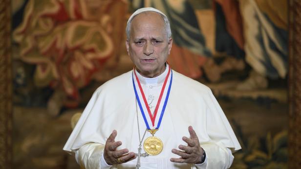 Papst Franziskus trägt die Philadelphia Liberty Medal um den Hals und spricht mit gestikulierenden Händen vor einem Wandteppich.