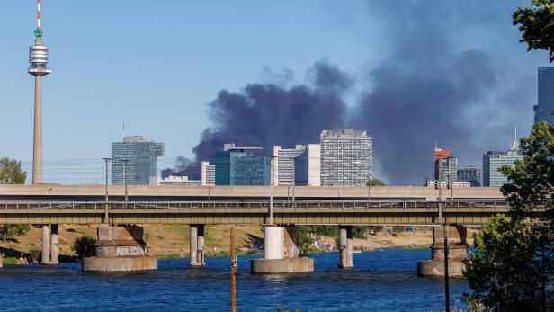 Eine dunkle Rauchwolke steigt hinter der Skyline der Wiener Donau City mit dem Donauturm auf.