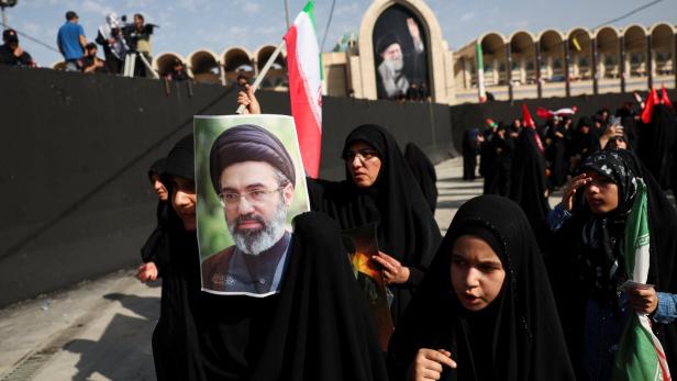 Frauen in schwarzen Tschadors halten bei einer Kundgebung im Iran Porträts von Ali Khamenei und iranische Flaggen in die Höhe.