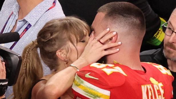 Taylor Swift küsst den Footballspieler Travis Kelce, der ein rotes Trikot der Kansas City Chiefs trägt.