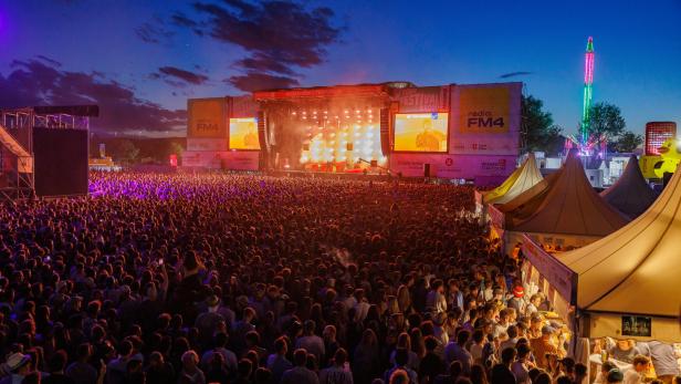 Eine große Menschenmenge versammelt sich bei Dämmerung vor der beleuchteten Wien Energie Festbühne beim Donauinselfest in Wien.