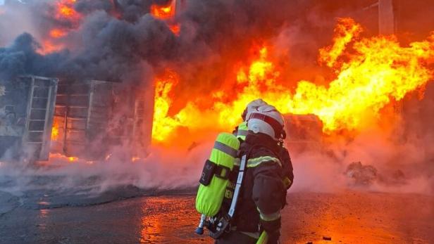 Feuerwehrmann vor einem brennenden Gebäude mit dichtem Rauch und meterhohen Flammen.