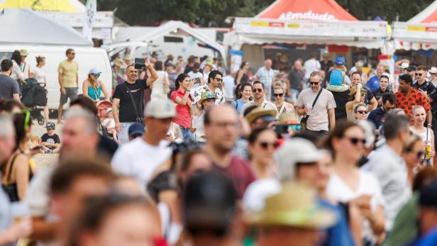 Menschenmenge auf einem Festival mit Ständen und Zelten im Hintergrund.