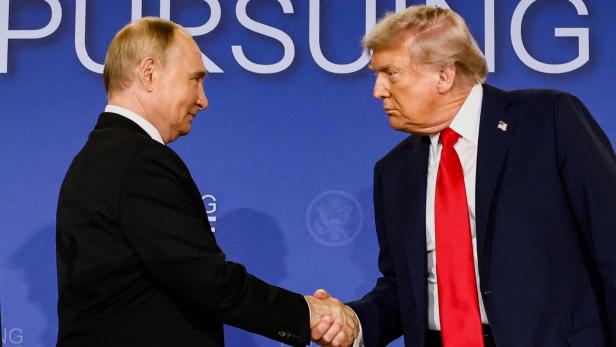 Wladimir Putin und Donald Trump schütteln sich vor blauem Gipfel-Hintergrund die Hand.